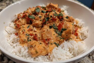 A close-up of One-Pot Creamy Tomato Basil Chicken and Rice served over fluffy white rice in a white bowl.