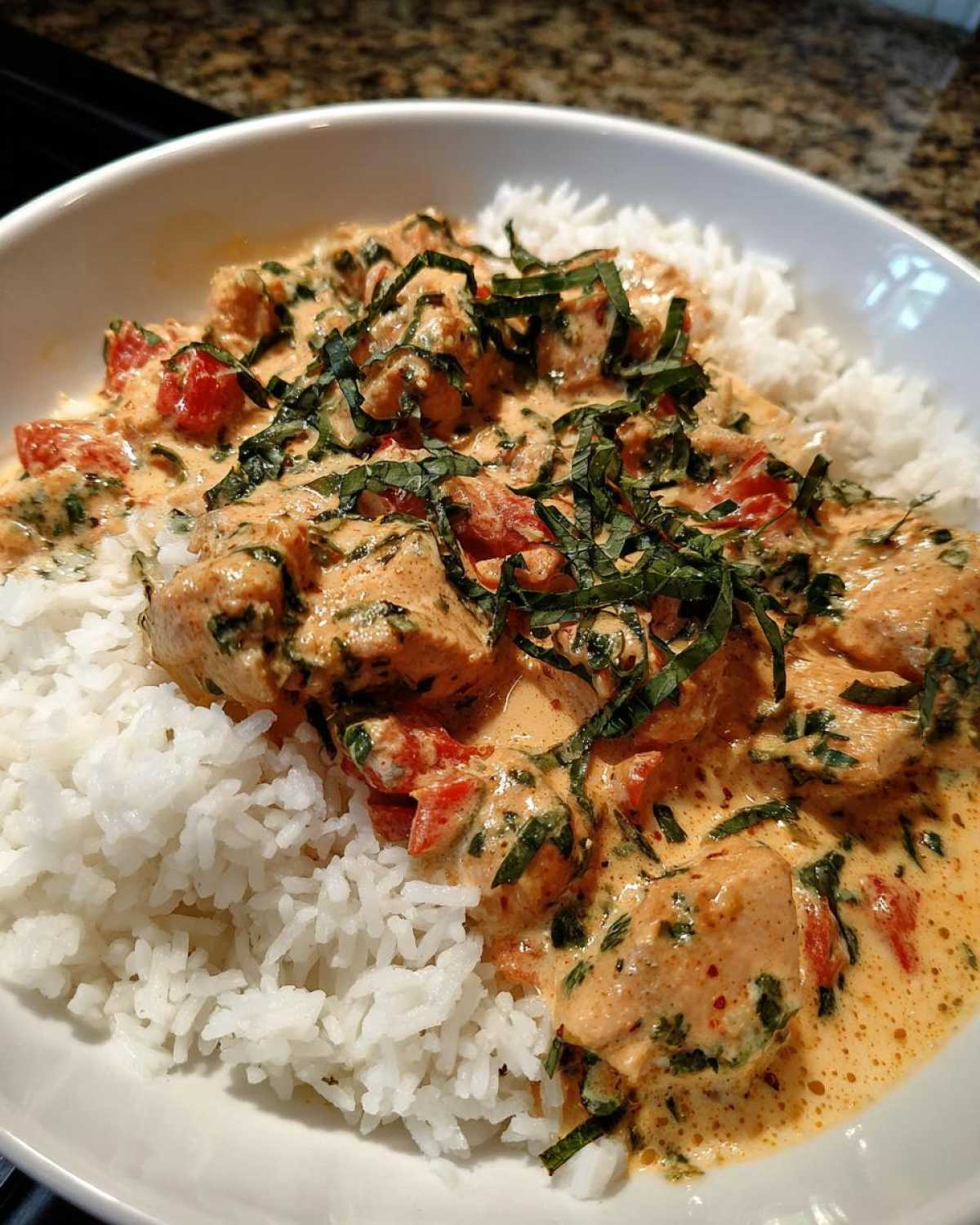A close-up of One-Pot Creamy Tomato Basil Chicken and Rice served over white rice, topped with fresh basil.