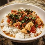 A close-up of One-Pot Creamy Tomato Basil Chicken and Rice served over white rice in a white bowl.