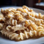 Close-up of fusilli pasta generously coated in rich Vegan Creamy Cashew Alfredo Sauce on a white plate.