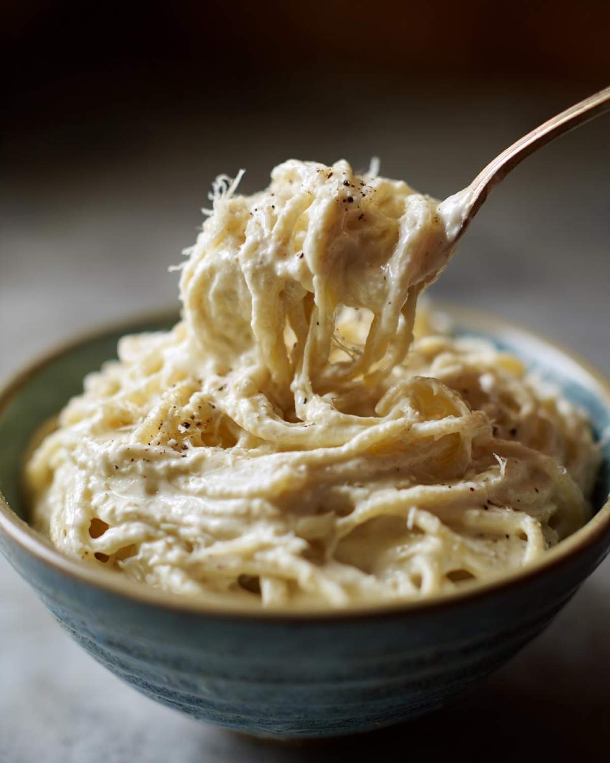 A fork lifting spaghetti coated heavily in Vegan Creamy Cashew Alfredo Sauce from a blue bowl.