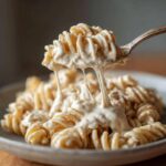 A spoonful of fusilli pasta coated in thick, creamy Vegan Creamy Cashew Alfredo Sauce, showing delicious cheese-like pulls.