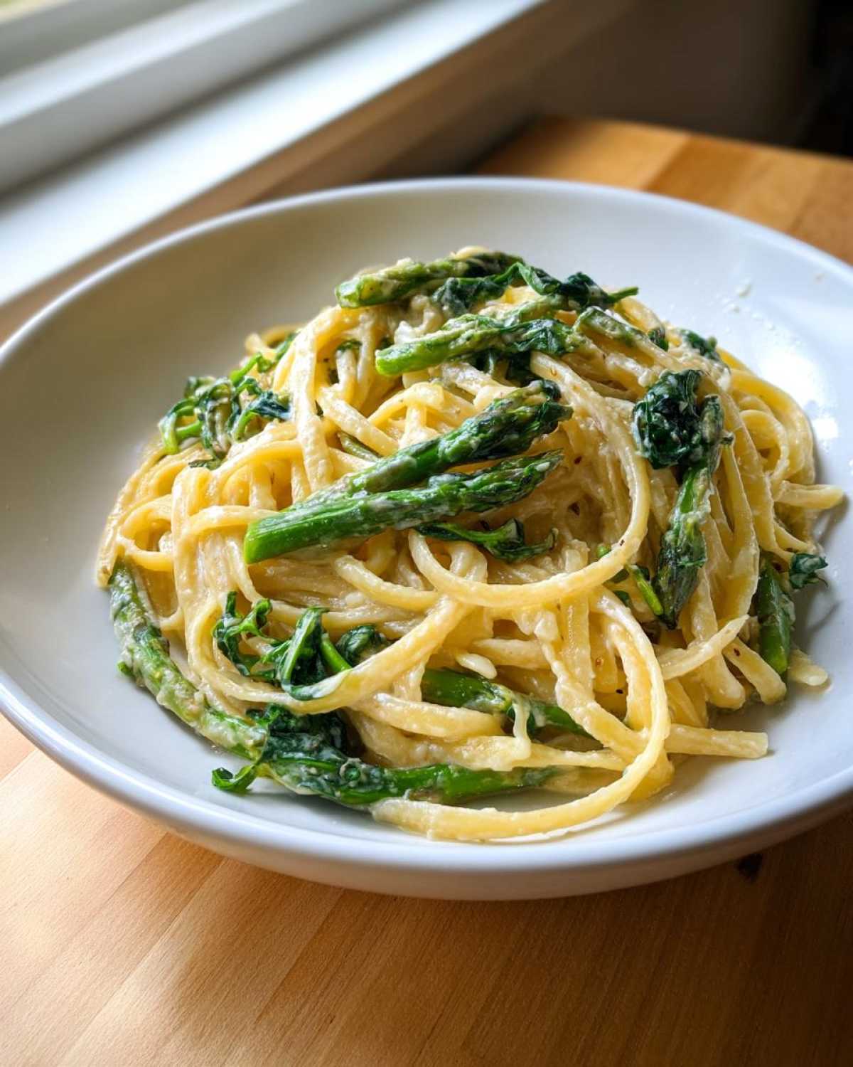 A close-up of creamy Vegan Lemon Asparagus Pasta tossed with bright green asparagus spears in a white bowl.