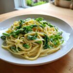 A close-up of Vegan Lemon Asparagus Pasta tossed in a creamy sauce and topped with bright green pea shoots.