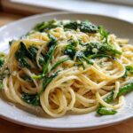 A serving of creamy Vegan Lemon Asparagus Pasta with bright green asparagus and pea shoots, topped with vegan parmesan.