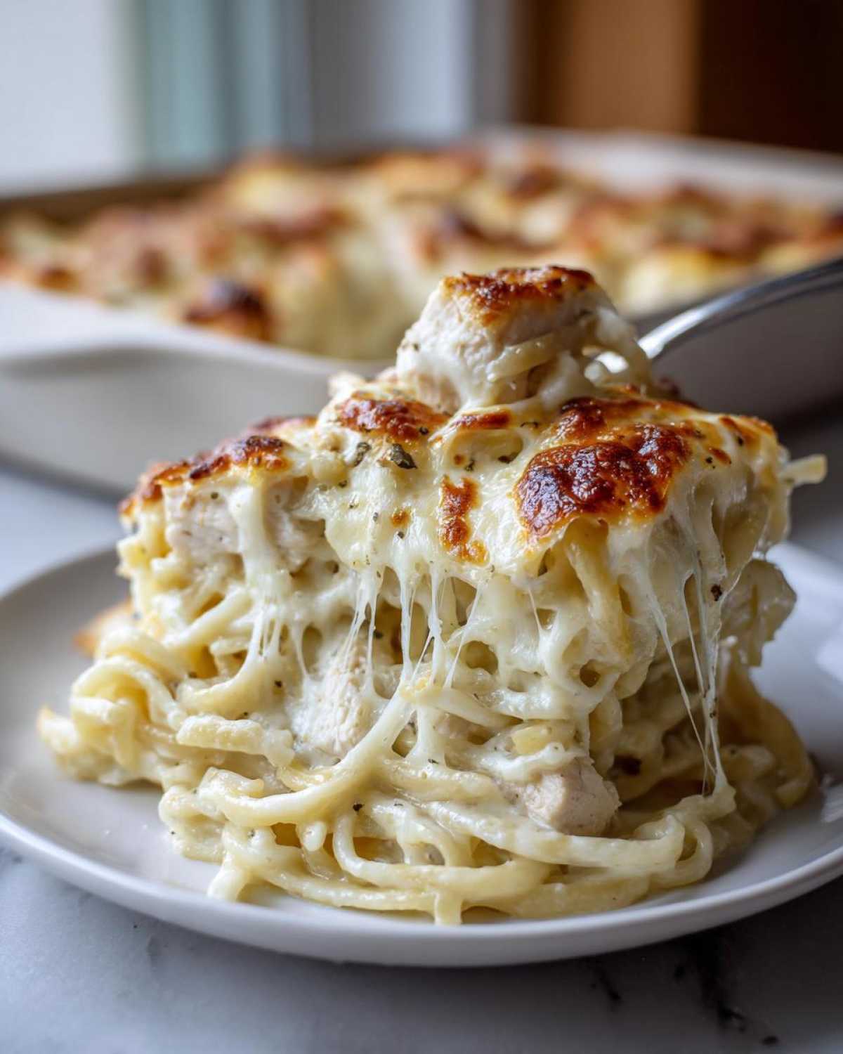 A serving of Cheesy Chicken Alfredo Bake with Mozzarella being lifted, showing long, stretchy cheese pulls.