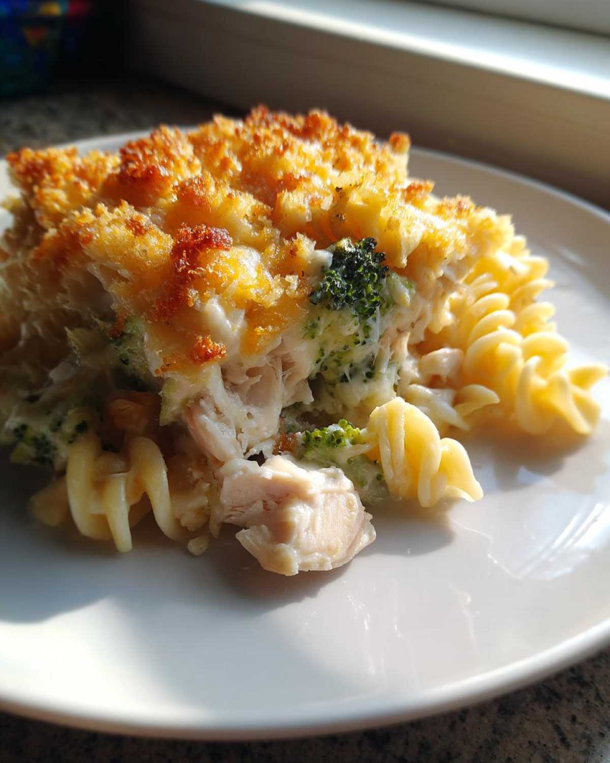 A close-up serving of Cheesy Chicken and Broccoli Pasta Bake with a crispy, golden topping.