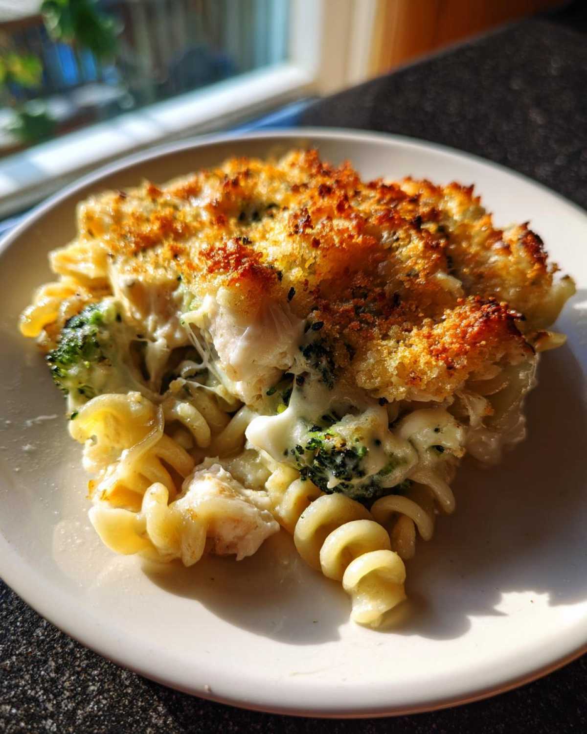A serving of Cheesy Chicken and Broccoli Pasta Bake with golden breadcrumbs on top, served on a white plate.