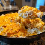 A spoonful of Cheesy Chicken and Rice Skillet with Cream Sauce showing melted, stretching cheddar cheese.