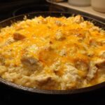 Close-up of a Cheesy Chicken and Rice Skillet topped with melted, golden cheddar cheese in a cast iron pan.