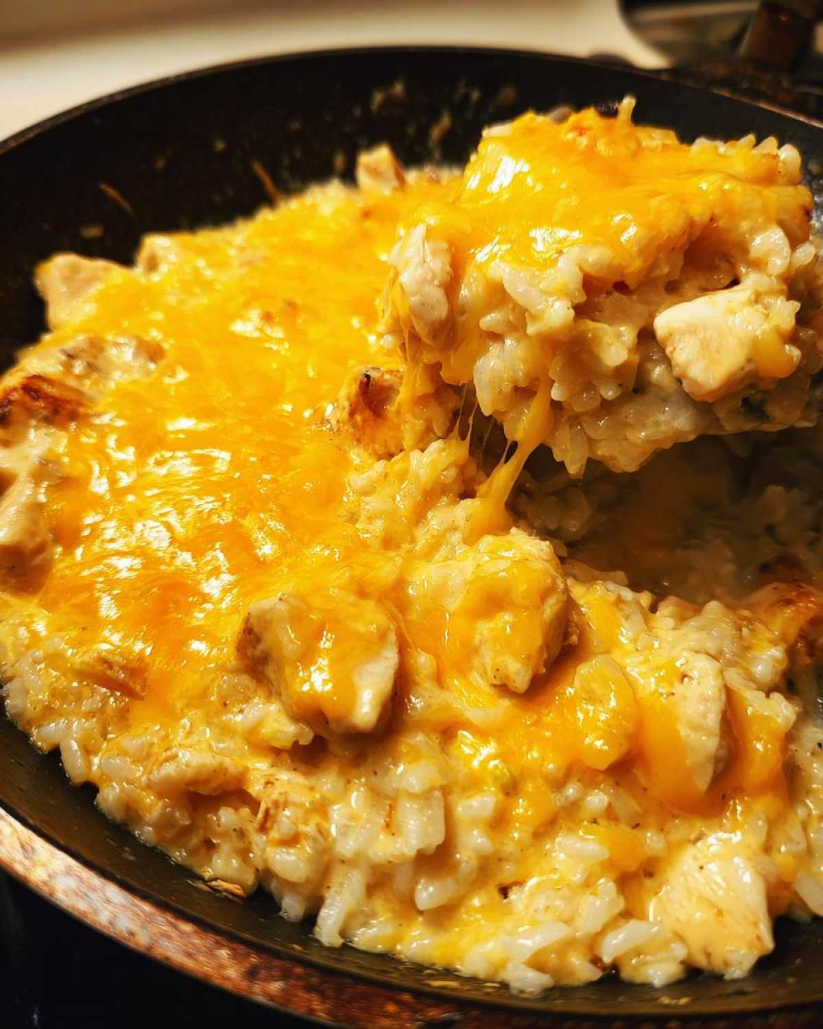 Close-up of Cheesy Chicken and Rice Skillet with a scoop being lifted, showing melted orange cheese.