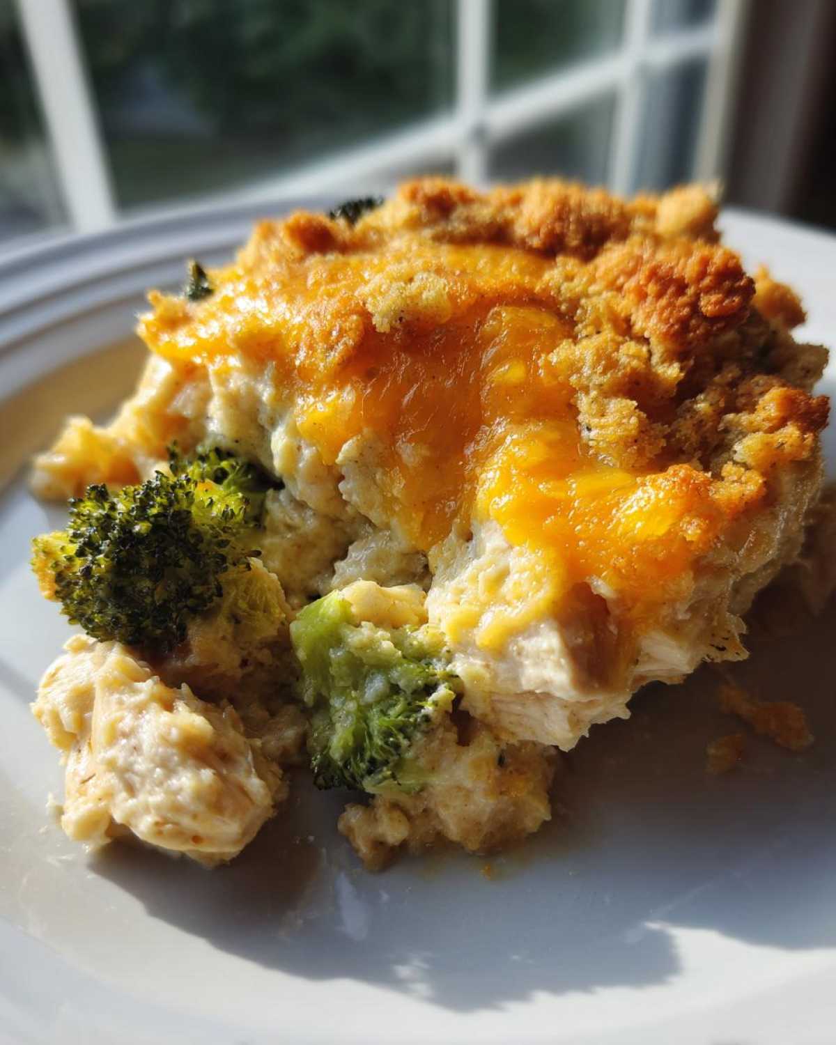 A close-up of a serving of Cheesy Chicken and Broccoli Bake Comfort Dish with melted cheddar cheese and a crunchy topping.