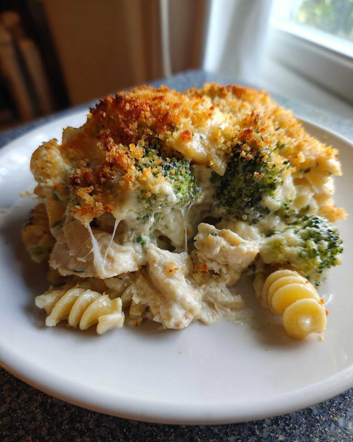 A close-up serving of Cheesy Chicken and Broccoli Pasta Bake with a golden, crispy topping and visible cheese pull.