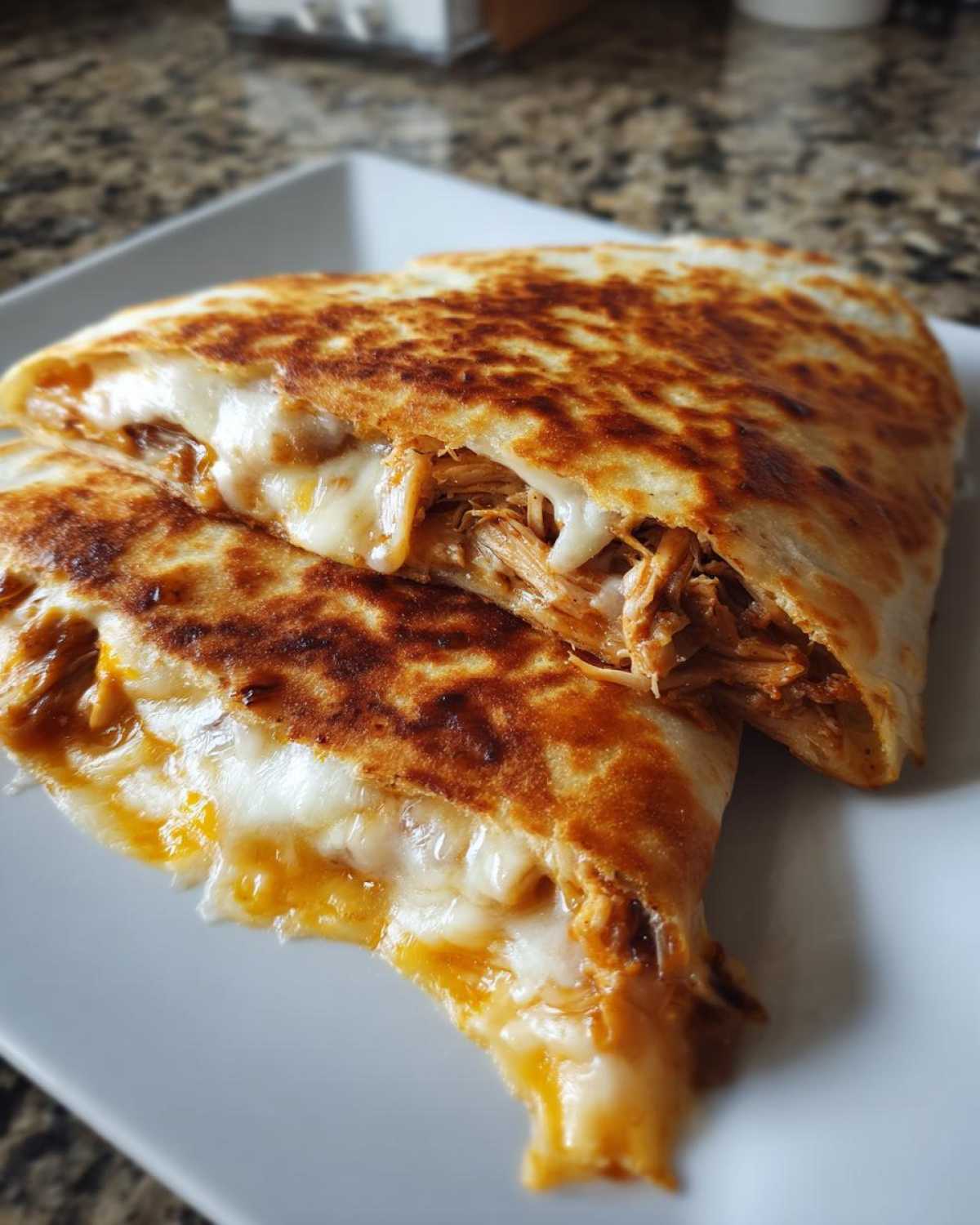 Close-up of a crispy Cheesy Chicken Quesadilla with crispy tortilla, cut in half, showing gooey melted cheese and shredded chicken filling.