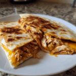 Two halves of a Cheesy Chicken Quesadilla with Crispy Tortilla showing melted cheese and shredded chicken filling.