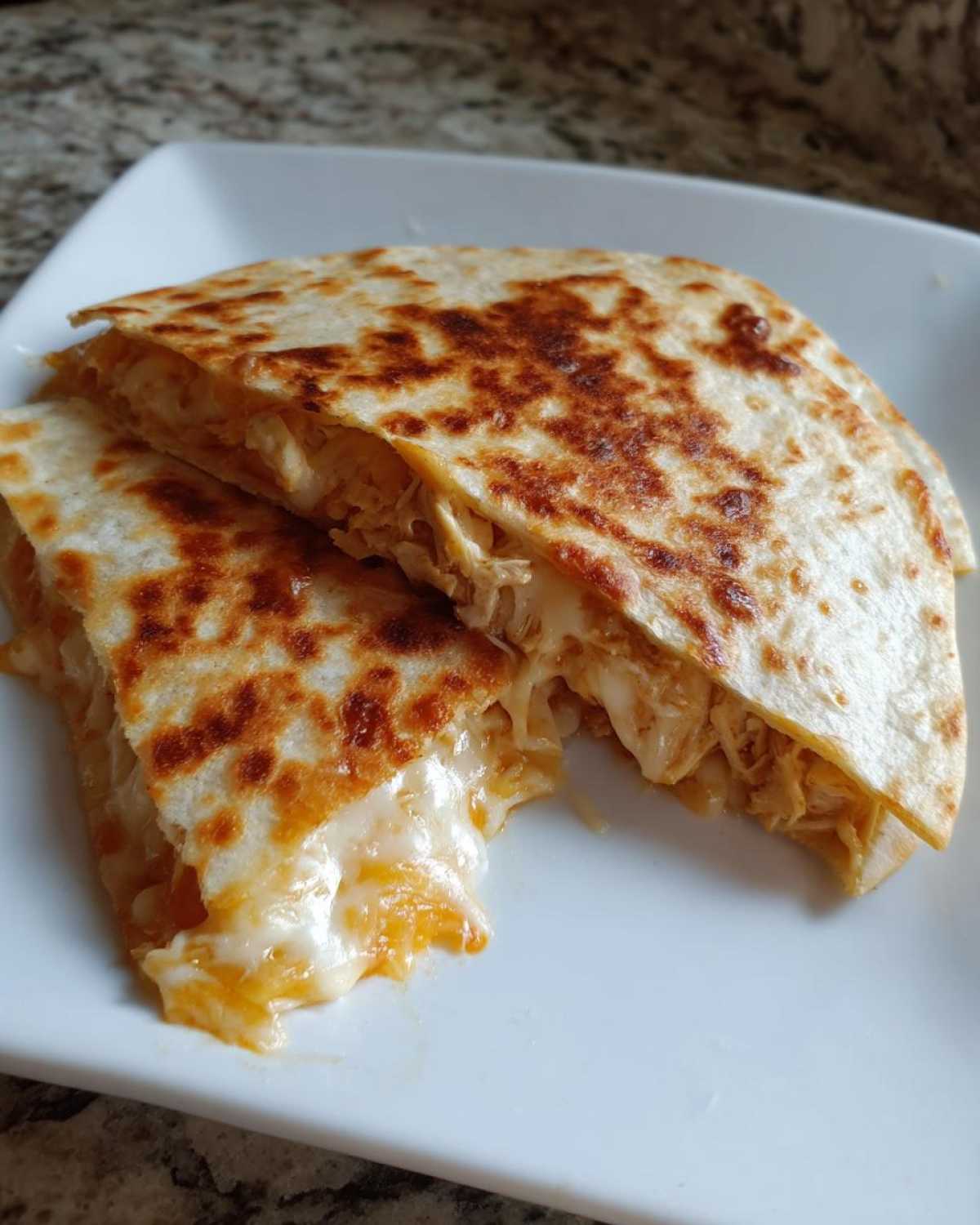 Two halves of a Cheesy Chicken Quesadilla with crispy tortilla showing melted cheese pull.