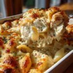 A spoonful of Cheesy Chicken Stuffed Pasta with Cream Sauce being lifted from a baking dish, showing melted cheese and filling.