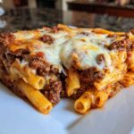 A close-up of a thick slice of Cheesy Ground Beef Pasta Bake with creamy sauce, topped with melted mozzarella.