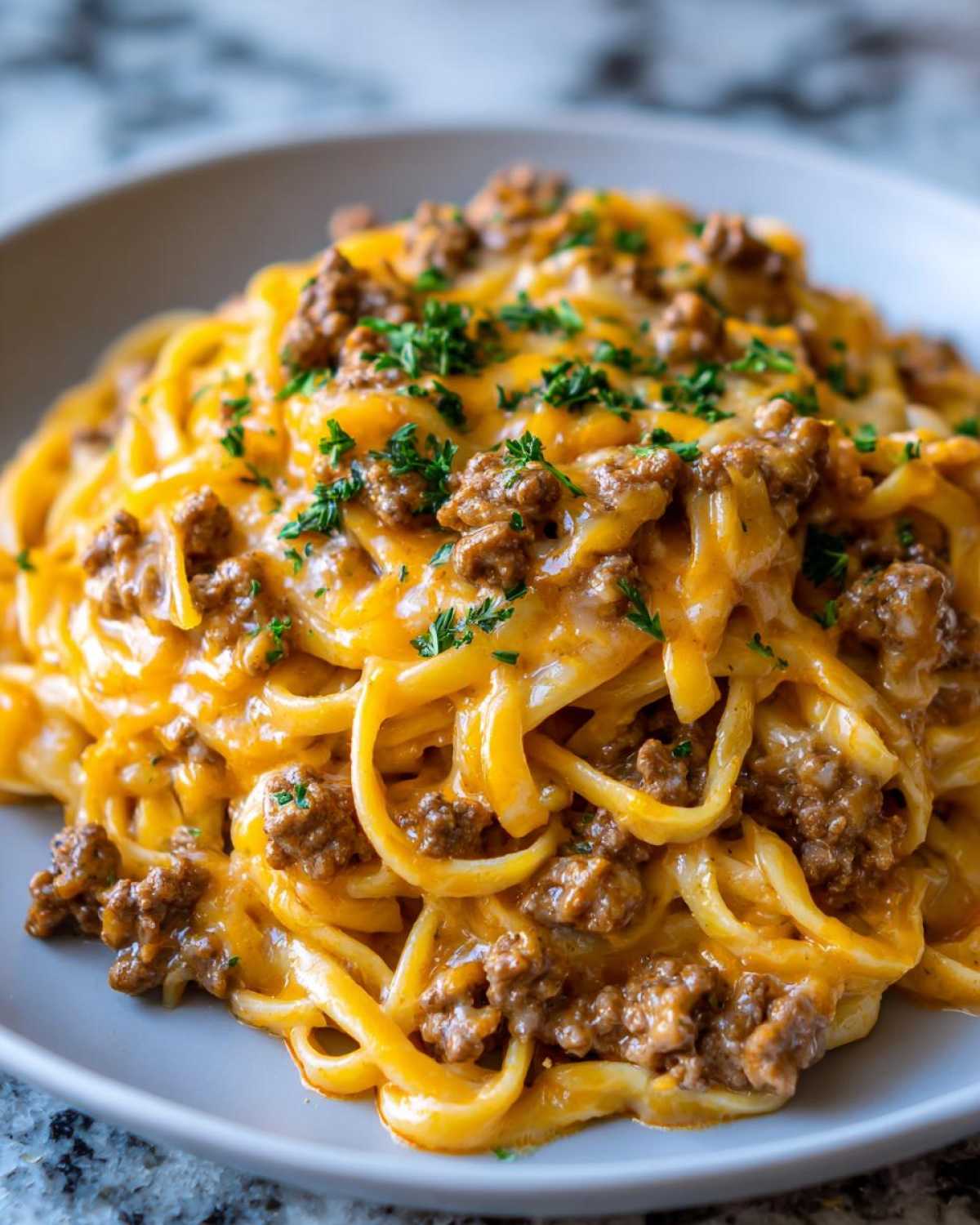 A close-up of a serving of Cheesy Ground Beef Pasta Skillet coated in a rich, orange cheese sauce and topped with fresh parsley.