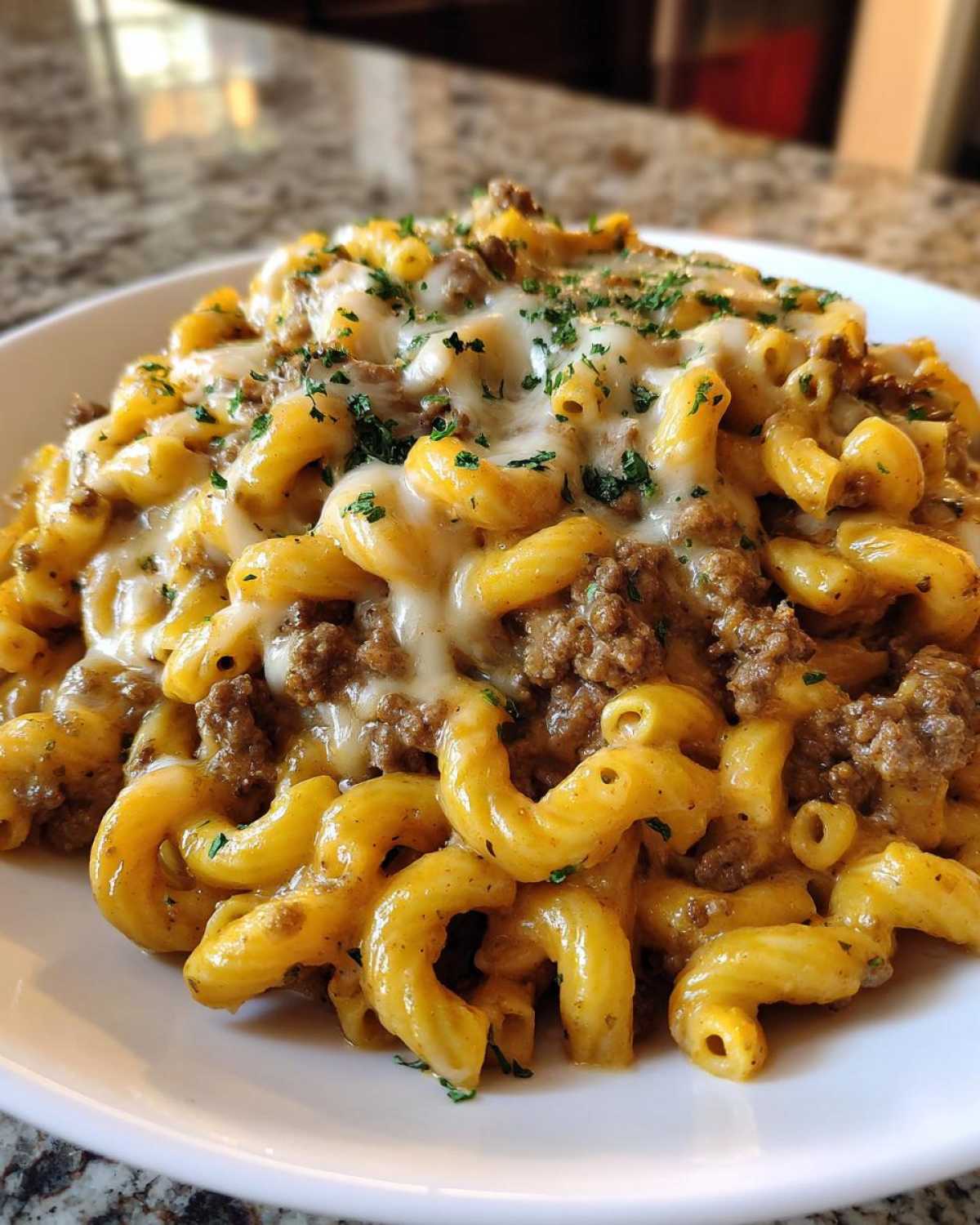 Close-up of a serving of Cheesy Ground Beef Pasta Skillet, featuring elbow macaroni coated in sauce, ground beef, and topped with melted white cheese and parsley.
