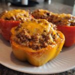 Close-up of baked Cheesy Ground Beef Stuffed Peppers, featuring a yellow pepper in the foreground topped with melted cheddar.