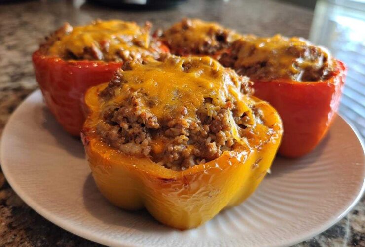 Close-up of baked Cheesy Ground Beef Stuffed Peppers, featuring a yellow pepper in the foreground topped with melted cheddar.