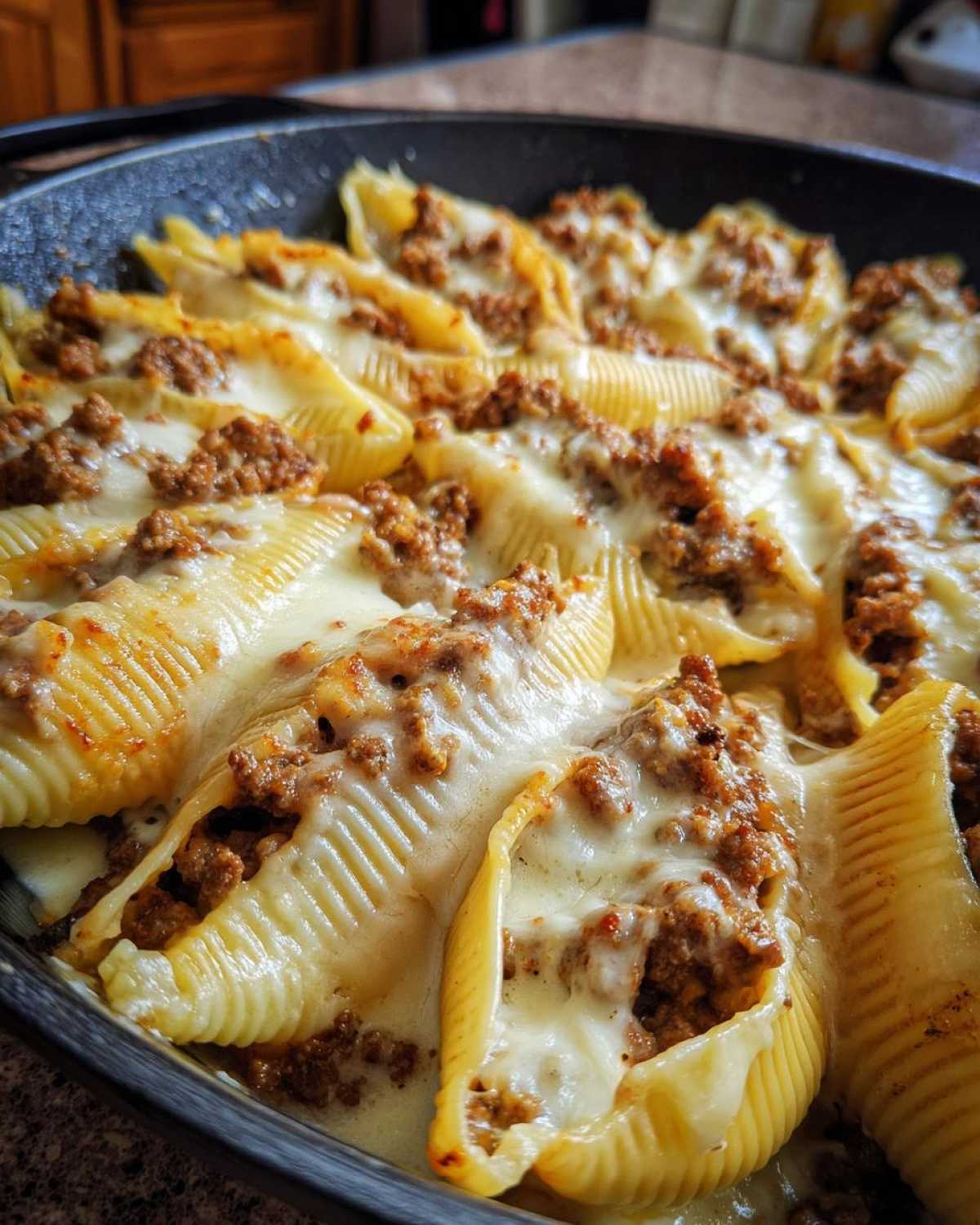 Close-up of baked Cheesy Ground Beef Stuffed Shells with melted mozzarella cheese in a black baking dish.