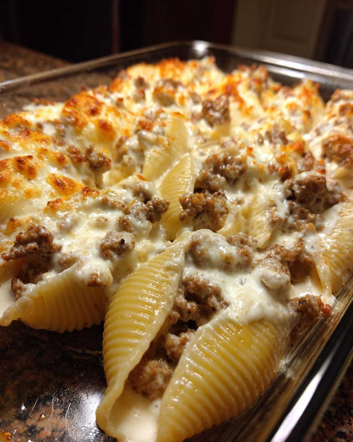 Close-up of baked Cheesy Ground Beef Stuffed Shells with Cream Sauce bubbling in a glass baking dish.