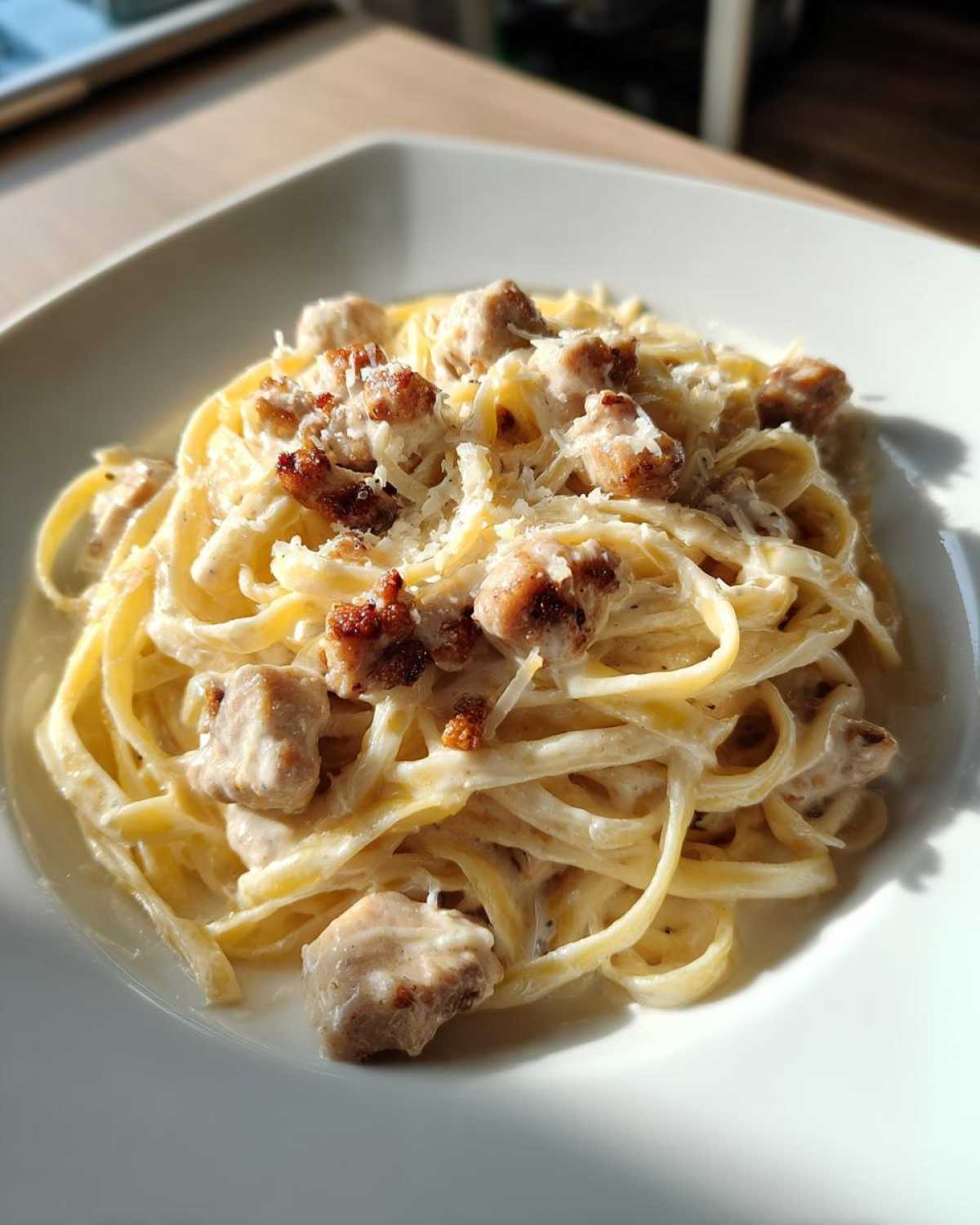 A close-up of creamy Alfredo chicken pasta featuring fettuccine noodles, chunks of seasoned chicken, and grated Parmesan cheese.