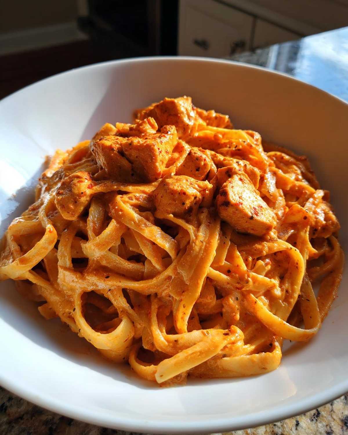 Close-up of a white bowl filled with rich and spicy Creamy Cajun Chicken Alfredo pasta, featuring fettuccine and seasoned chicken pieces.