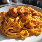 Close-up of Creamy Cajun Chicken Alfredo featuring fettuccine pasta coated in a rich, orange-hued sauce with chunks of seasoned chicken.