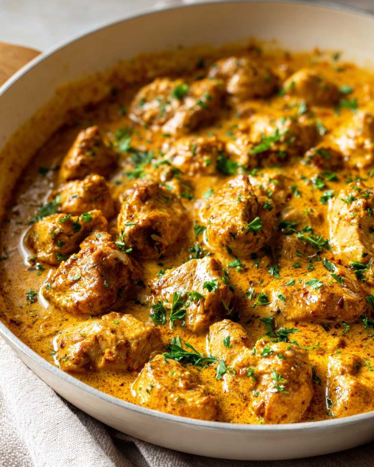 Close-up of bite-sized chicken pieces coated in a rich, orange-hued Creamy Cajun Chicken Skillet sauce, garnished with parsley.