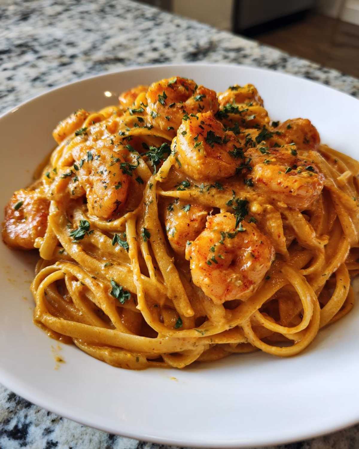 A close-up of rich, orange-hued Creamy Cajun Shrimp Pasta topped with seasoned shrimp and parsley.
