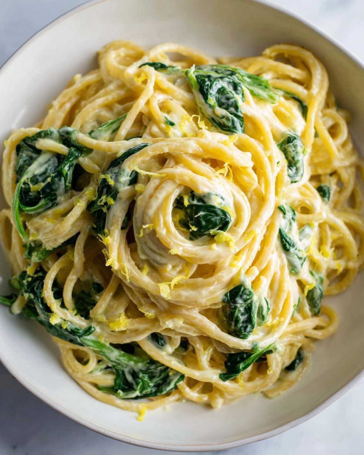 Close-up of Creamy Lemon Ricotta Pasta with Spinach tossed in a white bowl, topped with lemon zest.