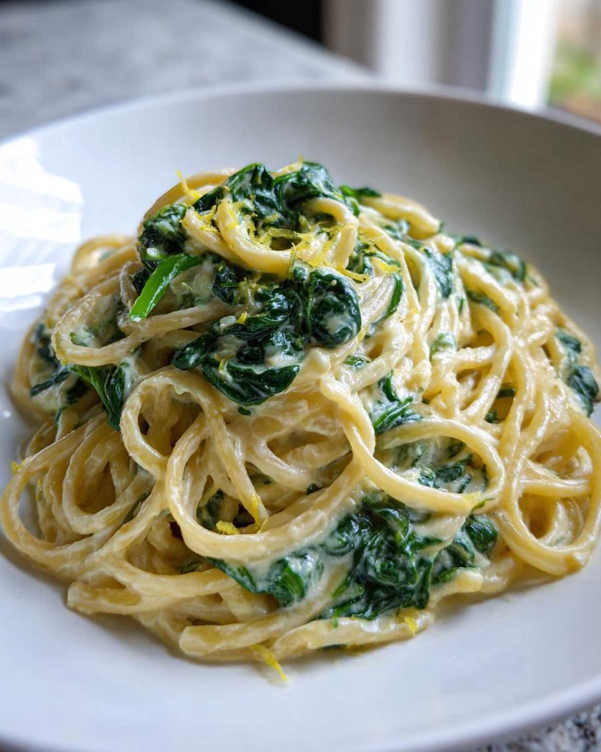 A close-up of Creamy Lemon Ricotta Pasta with Spinach tossed in a white bowl, topped with lemon zest.