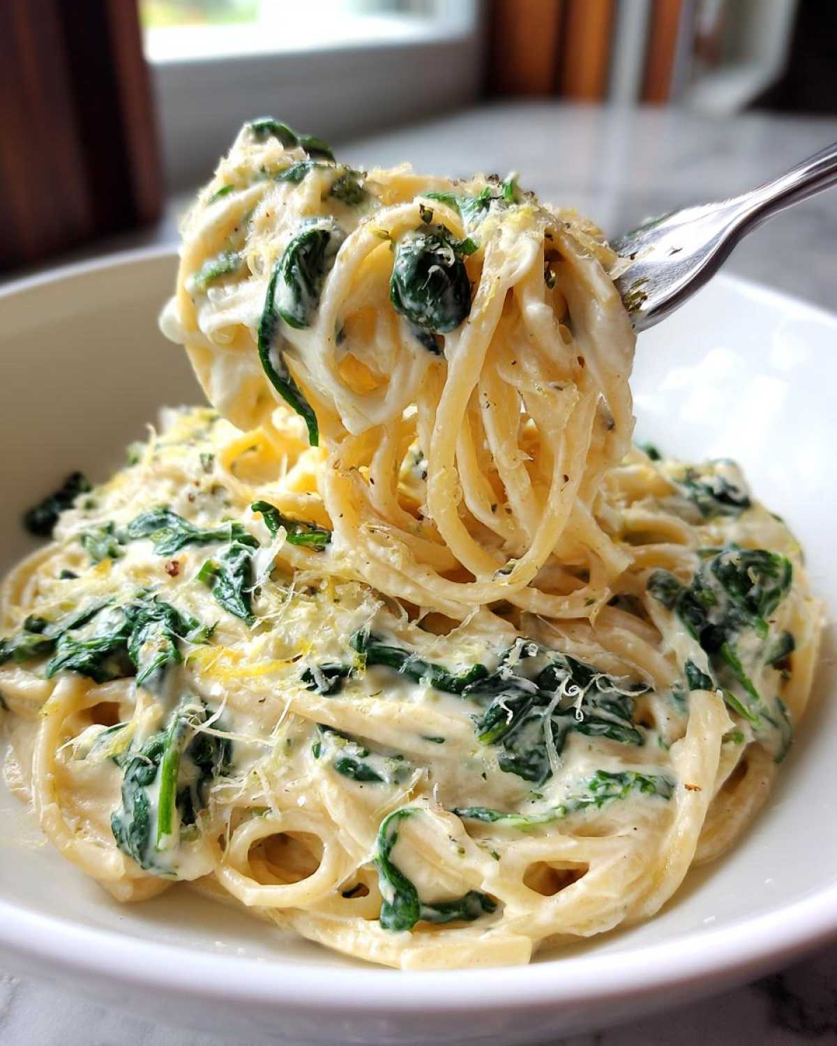 A fork lifting a swirl of Creamy Lemon Ricotta Pasta with Spinach coated in a rich white sauce and green spinach.
