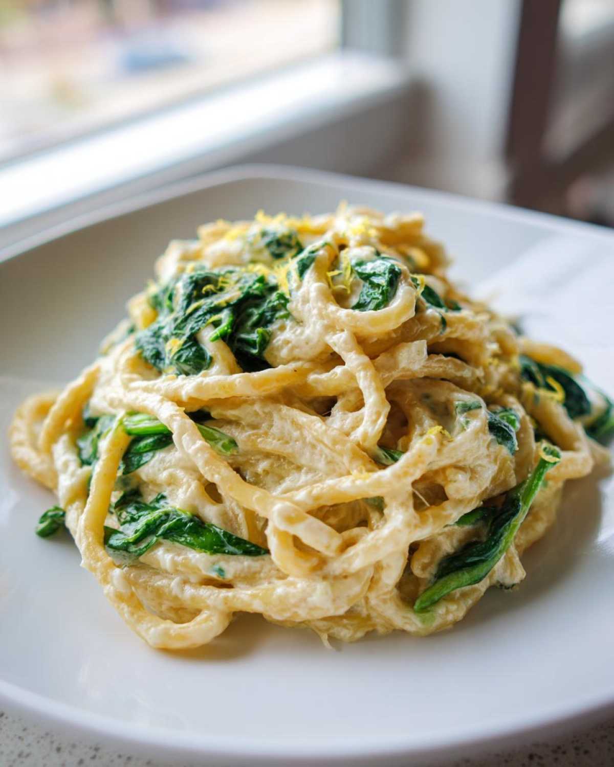 A close-up of Creamy Lemon Ricotta Pasta with Spinach tossed in a rich sauce and topped with lemon zest.