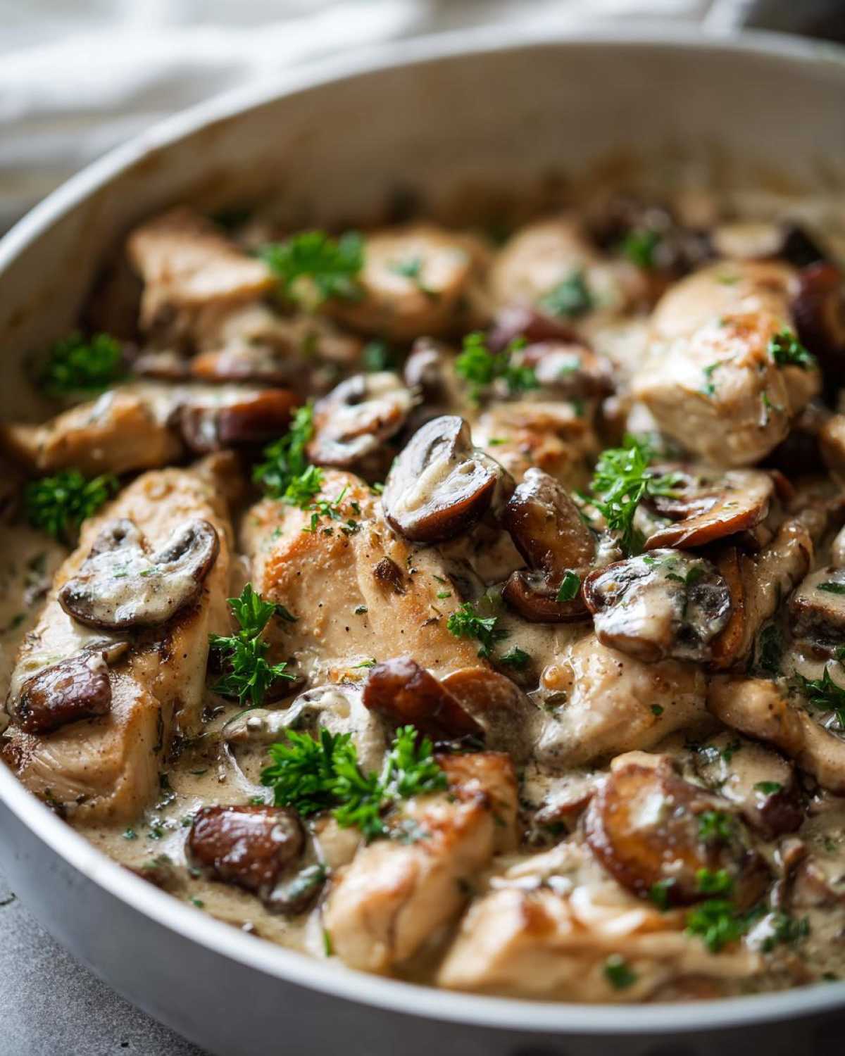 Close-up of seared chicken pieces covered in a rich, creamy mushroom alfredo sauce and garnished with fresh parsley.