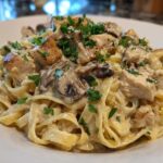 Close-up of rich Creamy Mushroom Chicken Alfredo Pasta featuring fettuccine, diced chicken, and sliced mushrooms, garnished with parsley.