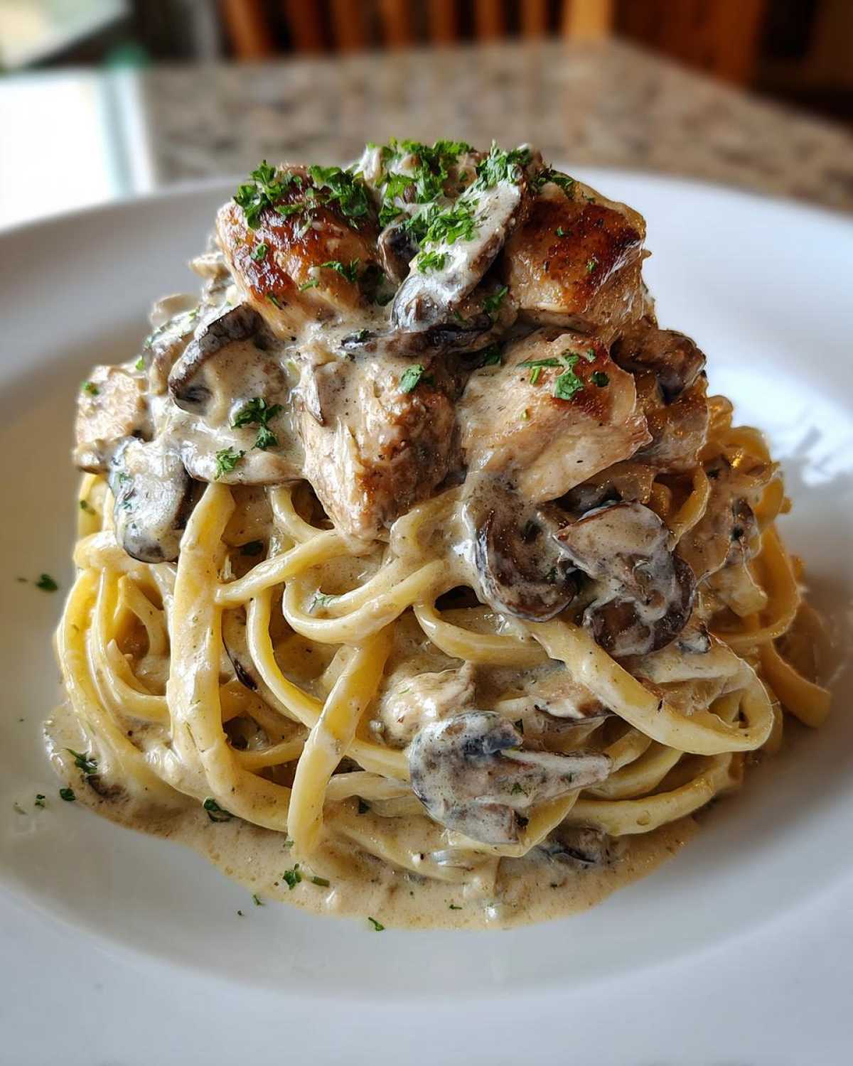 A tall serving of Creamy Mushroom Chicken Alfredo Pasta featuring fettuccine coated in rich sauce, topped with seared chicken pieces and mushrooms.