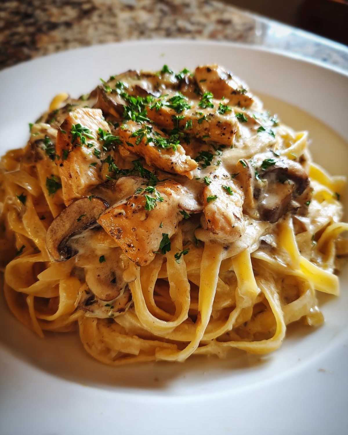 Close-up of a serving of Creamy Mushroom Chicken Alfredo Pasta with fettuccine noodles and fresh parsley garnish.