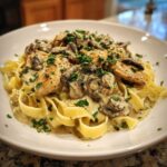 A serving of Creamy Mushroom Chicken Pasta with garlic sauce, featuring fettuccine, chicken pieces, and mushrooms, topped with parsley.
