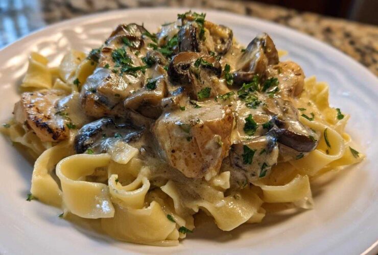 A close-up of Creamy Mushroom Chicken Pasta with Garlic Sauce served over egg noodles, garnished with parsley.