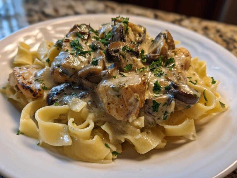 A close-up of Creamy Mushroom Chicken Pasta with Garlic Sauce served over egg noodles, garnished with parsley.