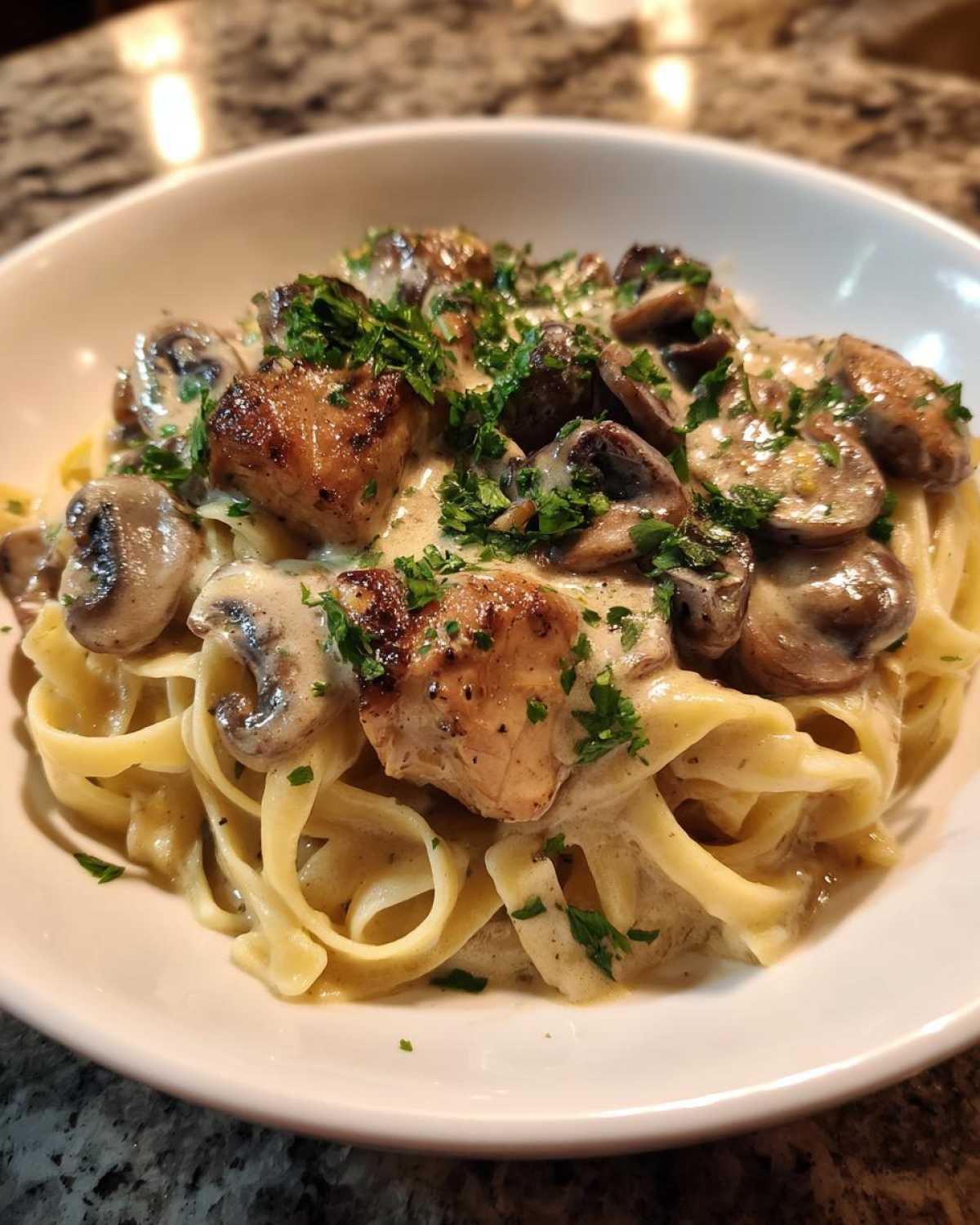 Close-up of a white bowl filled with Creamy Mushroom Chicken Pasta with Garlic Sauce, topped with parsley.