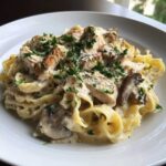 A close-up of Creamy Mushroom Chicken Pasta with Parmesan featuring fettuccine, sliced chicken, mushrooms, and parsley garnish.