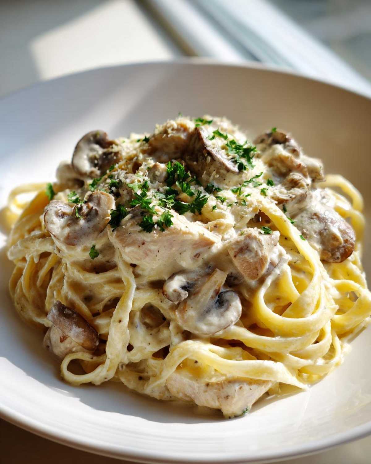 A close-up of creamy mushroom chicken pasta with parmesan cheese and fresh parsley garnish.