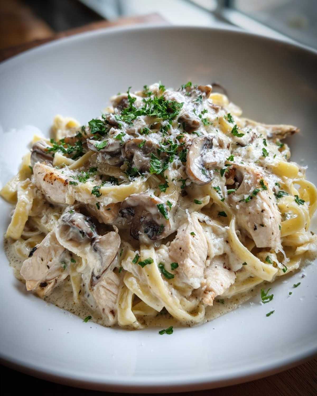 Close-up of a bowl of Creamy Mushroom Chicken Pasta with Parmesan, topped with fresh parsley.