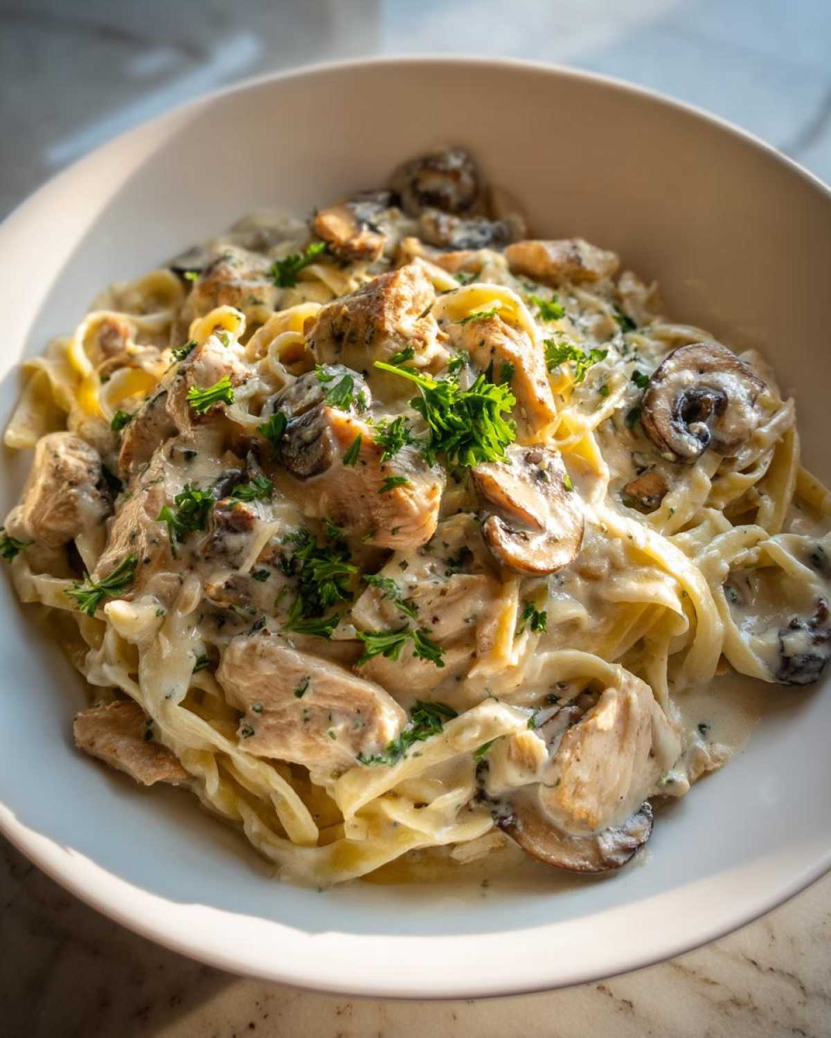 A close-up of a bowl filled with Creamy Mushroom Chicken Pasta with Parmesan, garnished with fresh parsley.