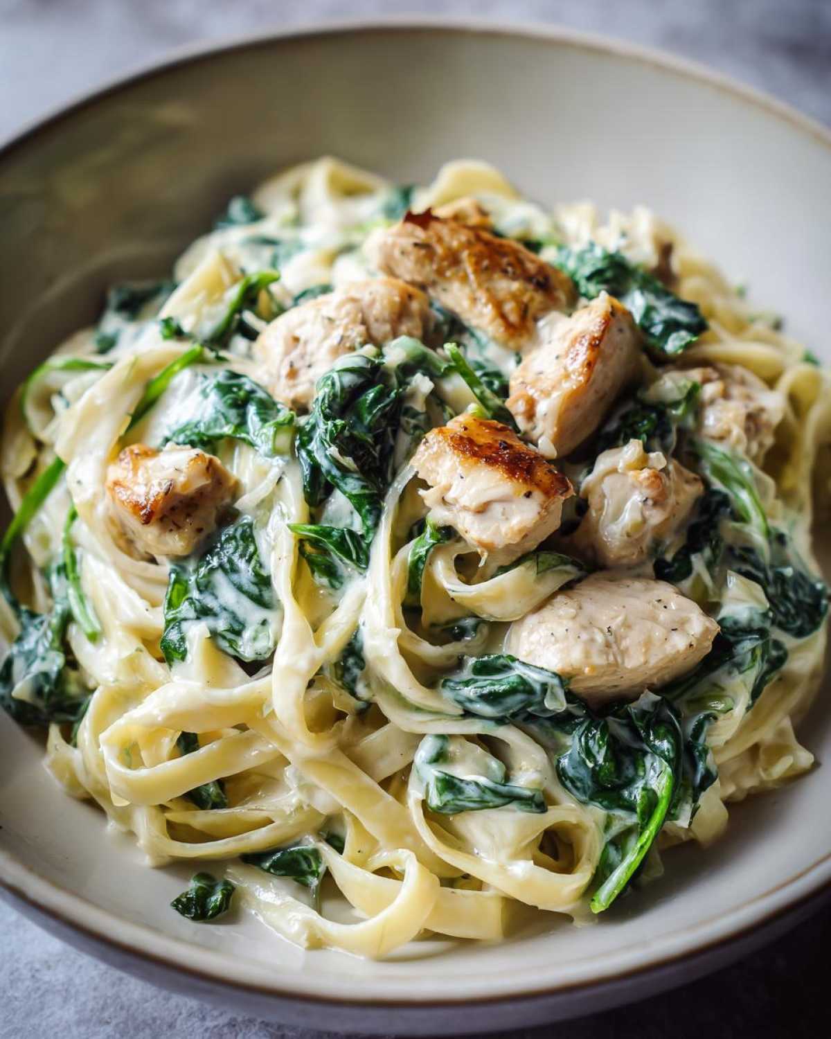 Close-up of a bowl filled with Creamy Spinach Chicken Pasta with Alfredo Sauce, featuring fettuccine, wilted spinach, and seared chicken pieces.